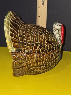 a ceramic turkey figurine sitting on top of a yellow table next to a ruler