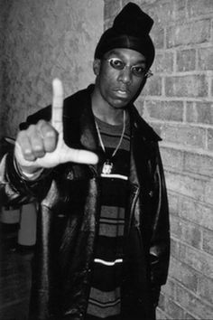 a young man pointing at the camera while standing in front of a brick wall with his finger up