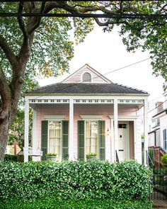 a small pink house with green shutters on the front door and white trim around the windows