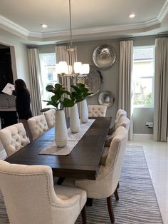 a dining room table surrounded by white chairs and vases with plants in them on top