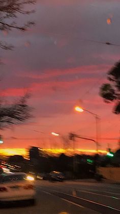 cars are driving down the street at dusk with colorful clouds in the sky behind them