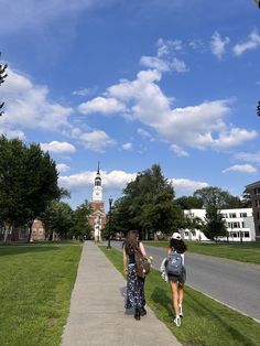 two women walking down a sidewalk in front of a building with a clock tower on it