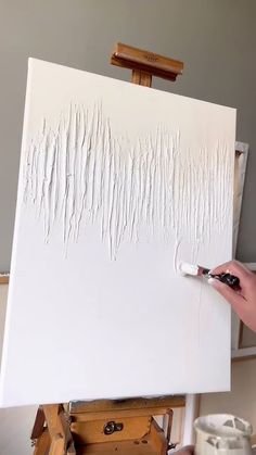 someone is painting on an easel with white paint