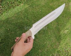 a person holding a knife in their hand on the grass with it's blade out