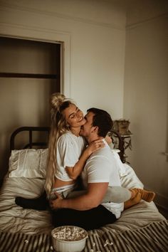 a man and woman sitting on top of a bed with popcorn in front of them