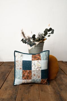 a potted plant sitting on top of a wooden table next to a pillow with a patchwork design