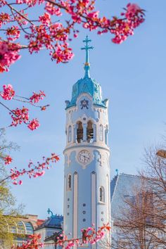 a tall white clock tower with a blue roof and cross on it's top