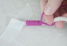 a person is tying a piece of string to a small white object with pink thread