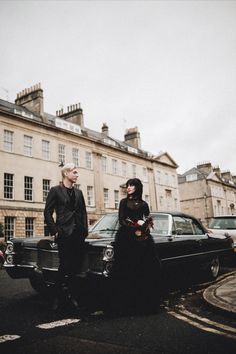 a man standing next to a woman in front of a car on a city street