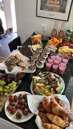 a table filled with lots of food on top of a black counter topped with fruit and pastries