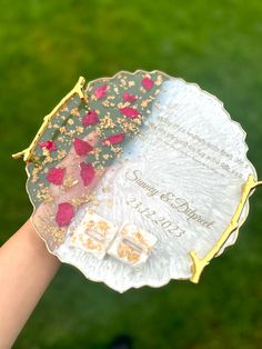 a hand holding a plate with flowers on it in front of a green lawn area