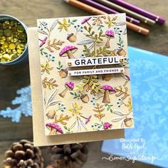 a handmade greeting card with mushrooms and pine cones on it, surrounded by other crafting supplies