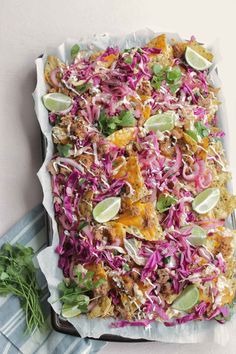 a dish with meat, cabbage and limes on a blue striped towel next to a fork