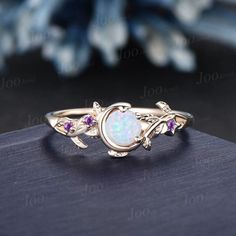 a white opal and pink sapphire ring sitting on top of a wooden table