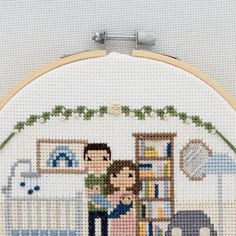 a cross stitch picture of a man and woman hugging in front of a baby crib