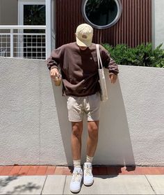 a man leaning against a wall with his hand on the back of his head and wearing a hat