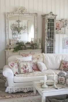 a living room filled with white furniture and flowers on the couch, coffee table and mirror