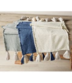 four different colors of towels hanging on a wooden rack with tassels and hooks