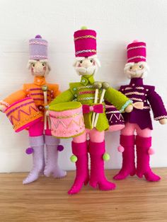 three dolls are dressed in brightly colored clothing and boots, one is holding a drum