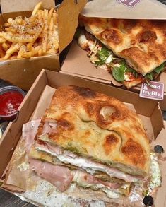 two boxes filled with sandwiches and fries on top of a wooden table next to each other