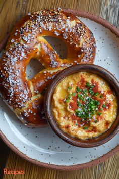 two pretzels on a plate with dip in the middle and another bagel to the side