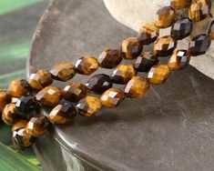 Showcasing rich, earthy colors, these tiger eye faceted rice beads impart both beauty and charm to your designs. They effortlessly shine with a chatoyant glow, perfect for any handcrafted jewelry destined for someone special. Sold as: 15-16" strand (approximately 50 beads per strand) No other stone evokes a big cat peering through the trees quite like Tiger Eye. Also known as Tiger's Eye stone, our Tiger Eye gemstone beads display lustrous, chatoyant stripes of brown and golden yellow. These beautiful stripes shimmer and change in different lighting conditions. This gives tiger eye beads such beautiful vibrancy and movement! Tiger Eye is especially common in South Africa, but can be found in various locations around the world. Tiger Eye is a fibrous variety of chalcedony that exhibits a pr Tiger Eye Gemstone, Enamel Beads, Rice Bead, Tigers Eye Gemstone, Large Hole Beads, Tiger Eye Beads, Eye Beads, Beads Online, Bead Store