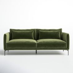 a green couch with two pillows on the back and one pillow on the side, in front of a white wall