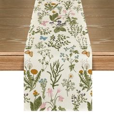 a white table runner with flowers and leaves on it, hanging from a wooden rail