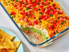 a casserole dish with tomatoes, cheese and tortilla chips on the side