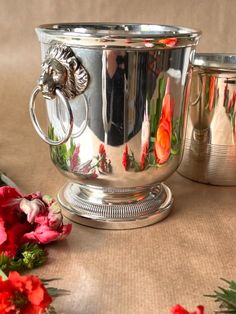 two silver cups sitting on top of a table next to flowers