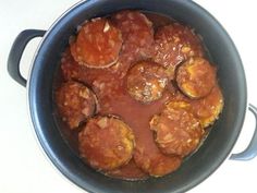 a pot filled with meatballs and sauce on top of a white counter next to a knife