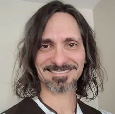 a man with long hair and a beard smiles at the camera while wearing a vest