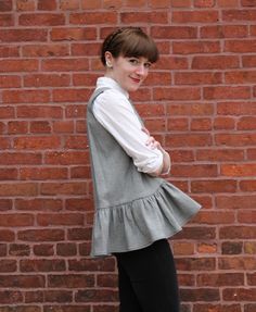 a woman standing in front of a brick wall wearing black pants and a white shirt