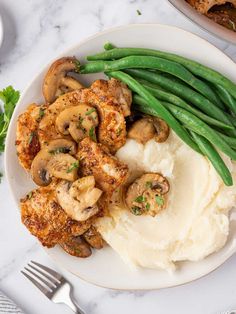 a plate with mashed potatoes, green beans and mushrooms on it next to a fork