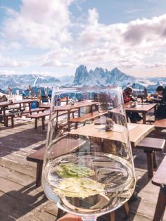 a glass of wine sitting on top of a wooden table next to benches and tables