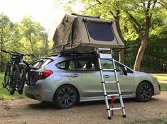 a car with a tent on the roof and bike rack attached to it's trunk