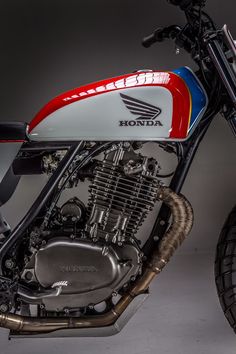 a red, white and blue motorcycle parked in a room with dark walls behind it