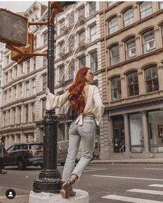 a woman standing on the corner of a street next to a traffic light and tall buildings