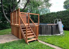 a wooden deck next to a hot tub in a yard with green grass and trees