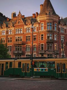 a green and yellow trolley is parked in front of an old brick building with many windows