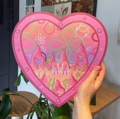 a person holding up a pink heart shaped paper plate in front of a potted plant