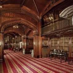 an ornately decorated library with red and gold carpeting, chandeliers and tables