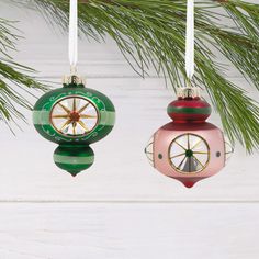 two ornaments hanging from a christmas tree on a white wooden background with pine branches in the foreground