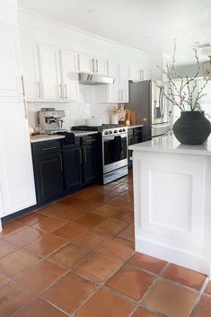 a kitchen with black and white cabinets, tile flooring and an island in the middle