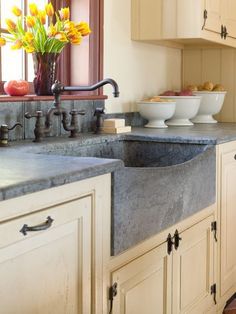 a kitchen with white cabinets and gray counter tops, bowls on the sink and yellow flowers in vases