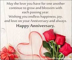 two roses and a heart on a white wooden background with the words happy anniversary written below