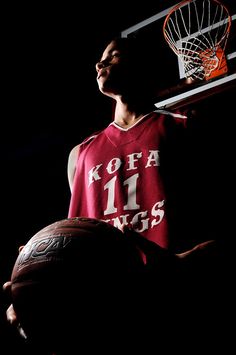 a man holding a basketball in his right hand and wearing a red shirt with white letters on it