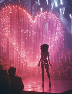 a woman is walking down the runway in front of a heart - shaped backdrop with fireworks