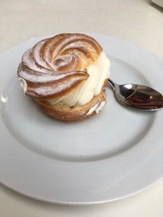 a white plate topped with a pastry covered in icing and powdered sugar next to a spoon