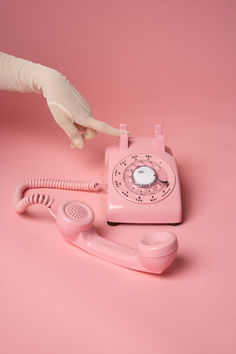 an old pink phone is being held up by a gloved hand on a pink background